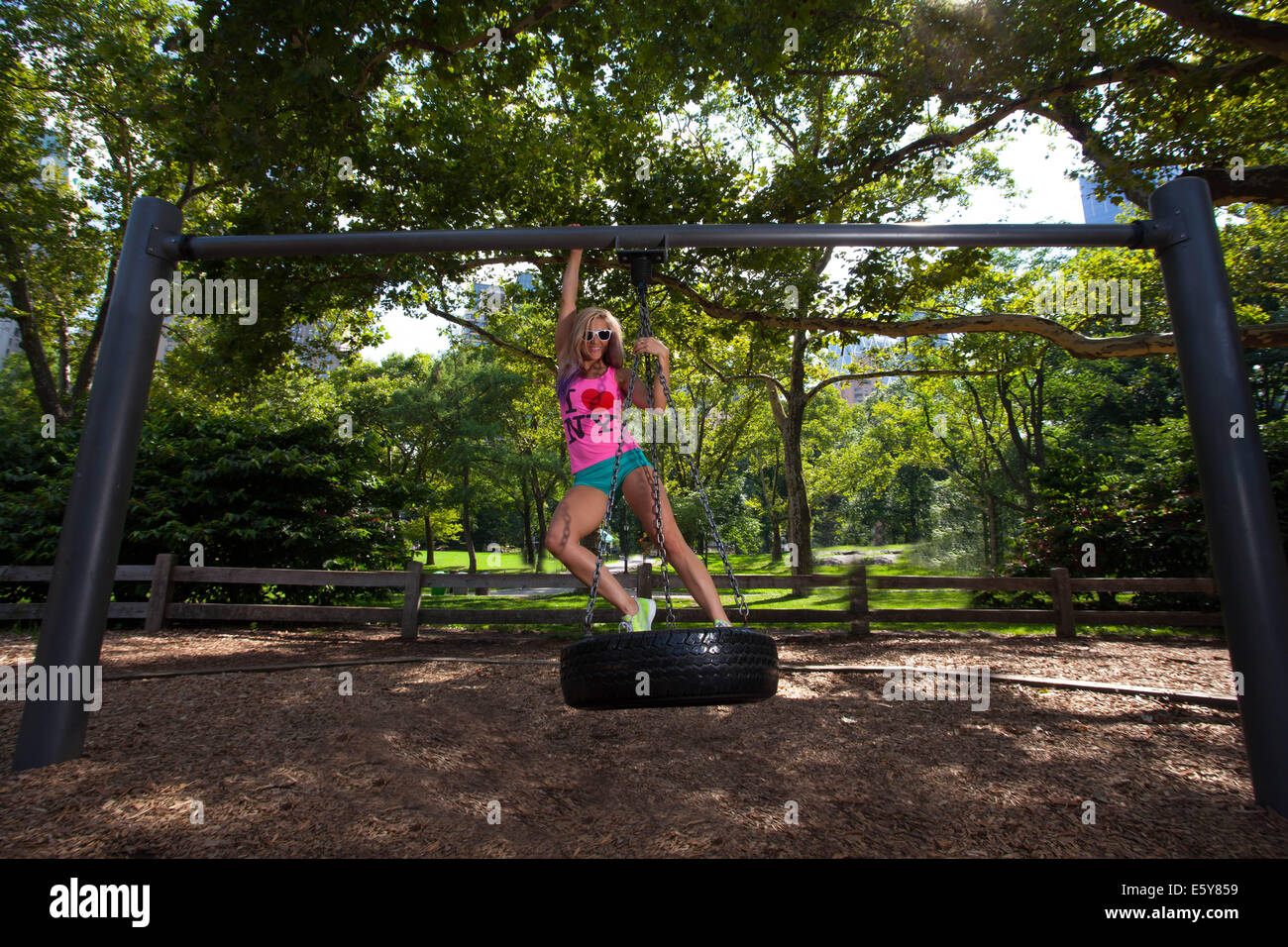 Young Blond Athletic woman sitting and rocking on a tire swing in