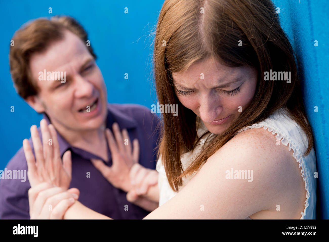 Aggressive man displaying violent behaviour and verbal abuse towards a helpless woman. Stock Photo