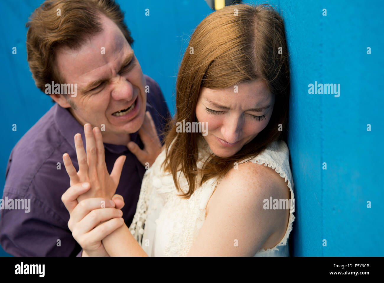 Aggressive man displaying violent behaviour and verbal abuse towards a helpless woman. Stock Photo