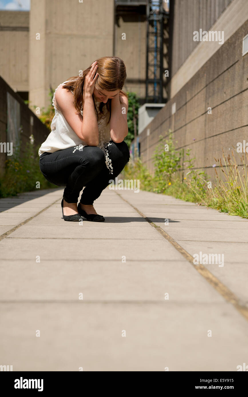 Stressed/tearful young woman,crouching down with her head in her hands. Stock Photo