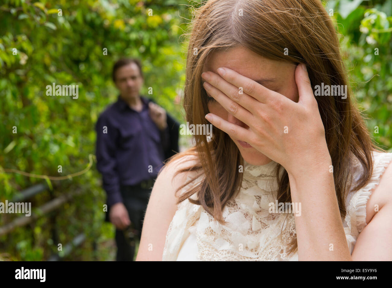 Tearful woman with hand on her face and man standing in the background. Stock Photo