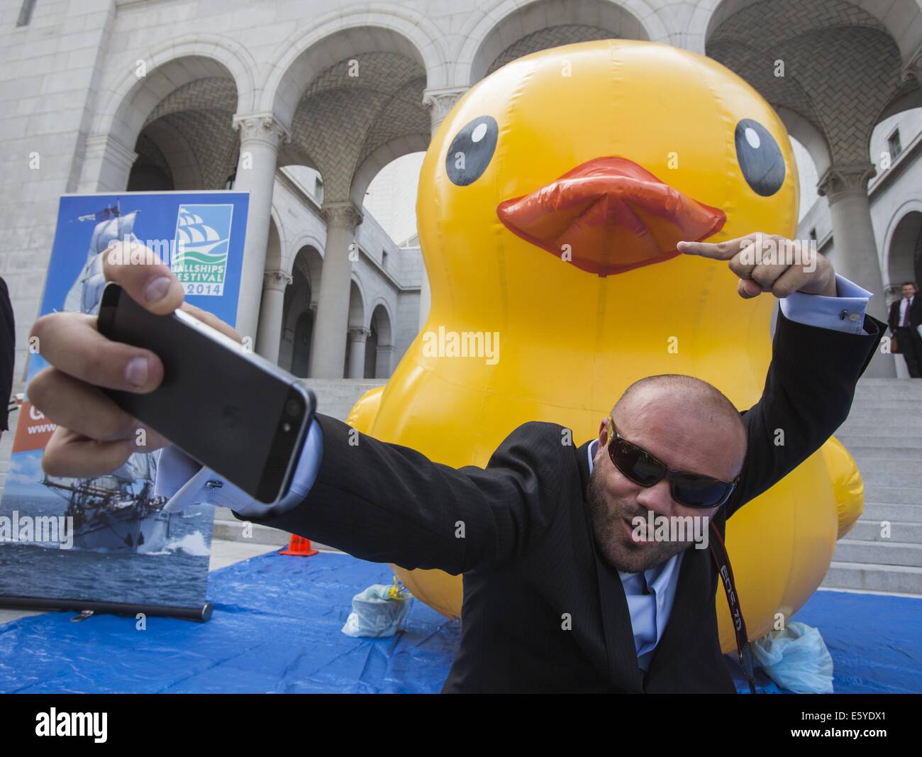 Los Angeles, California, USA. 8th Aug, 2014. Branimir Kvartuc poses for a selfie with a 10-foot-tall rubber ducky ''baby duck'' squatting on the Spring Street steps of Los Angeles City Hall on Friday, Aug. 8, 2014, in Los Angeles. The bright yellow, inflatable ducky is wandering the city in search of its mother, a 60 feet high and dubbed by event organizers as the world's largest rubber ducky as part of a promotional stunt for the Tall Ships Festival taking place Aug. 20-24 at the Port of Los Angeles. Credit:  Ringo Chiu/ZUMA Wire/Alamy Live News Stock Photo