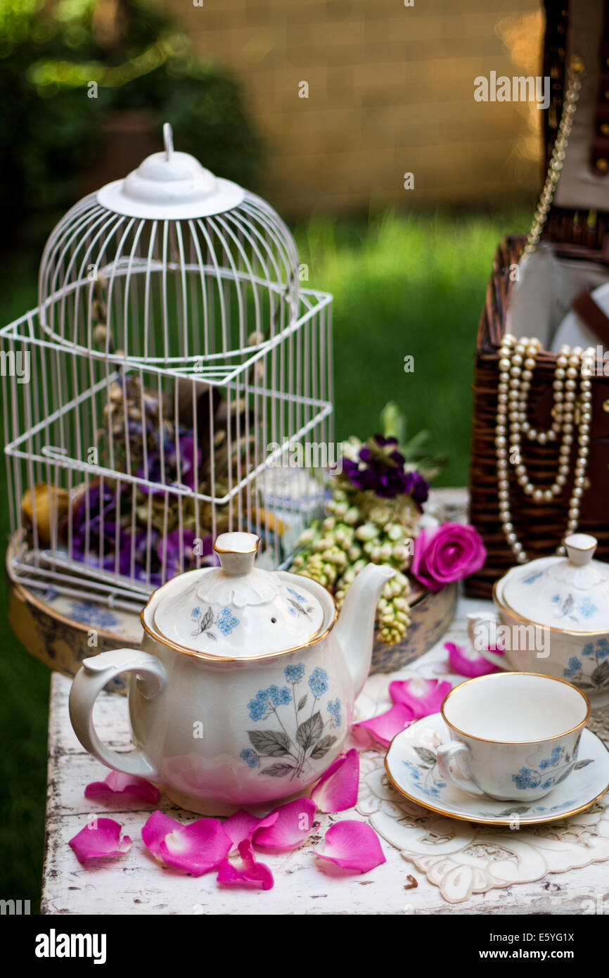 Old fashioned British tea set in the garden with petals and flowers Stock Photo
