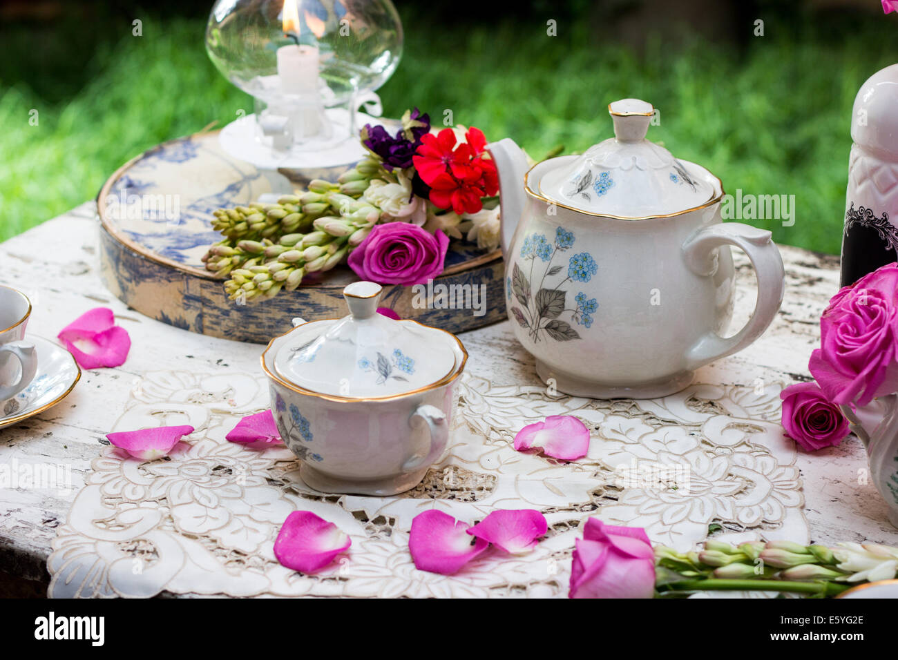 Old fashioned tea set in the garden with petals and flowers Stock Photo