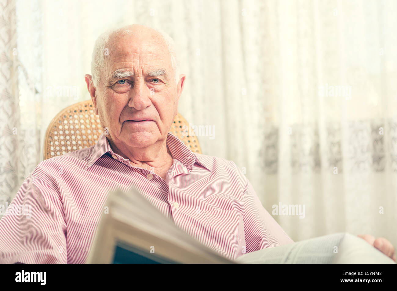 Elderly man sitting on chair reading newspaper at home Stock Photo - Alamy
