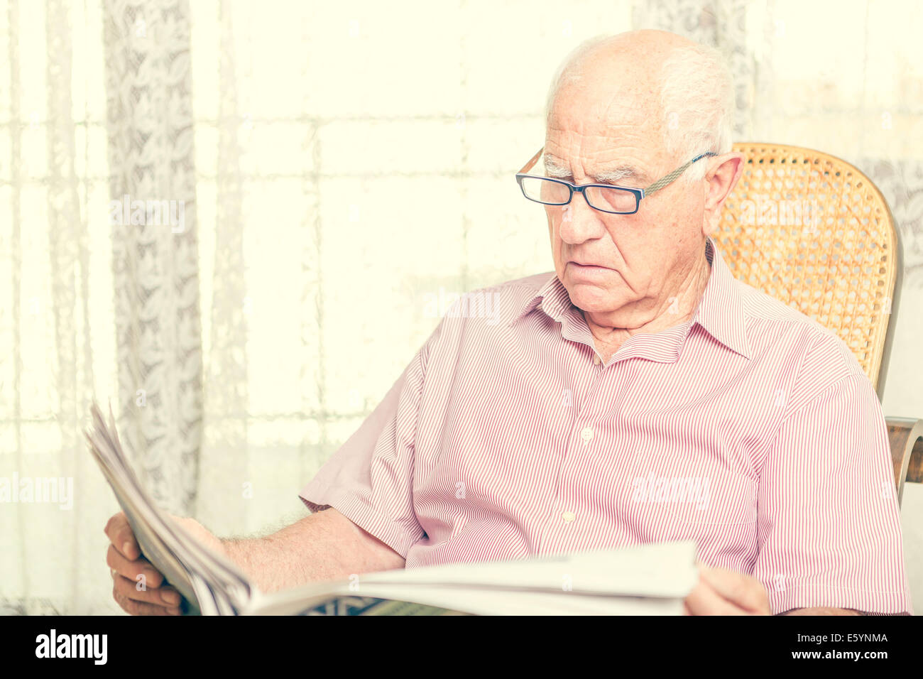 Elderly man sitting on chair reading newspaper at home Stock Photo - Alamy