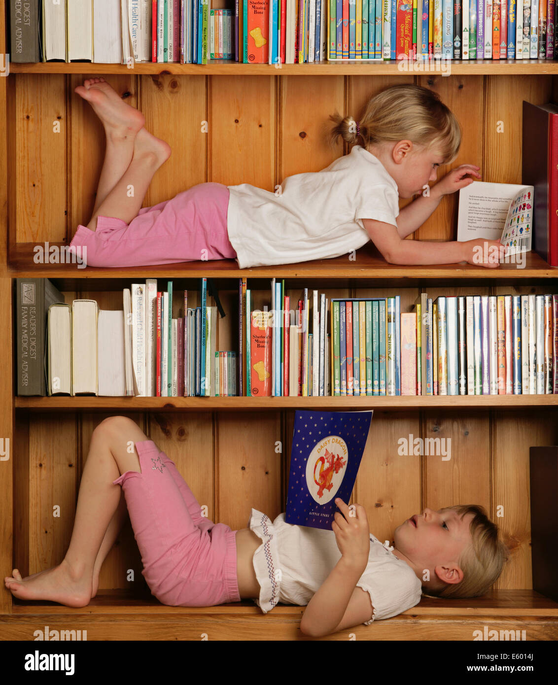 Young girls reading books whilst lying in a bookcase Stock Photo
