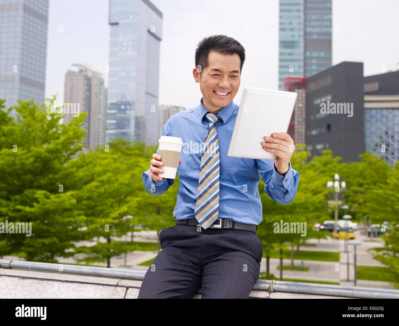 asian businessman looking at tablet holding coffee cup smiling. Stock Photo