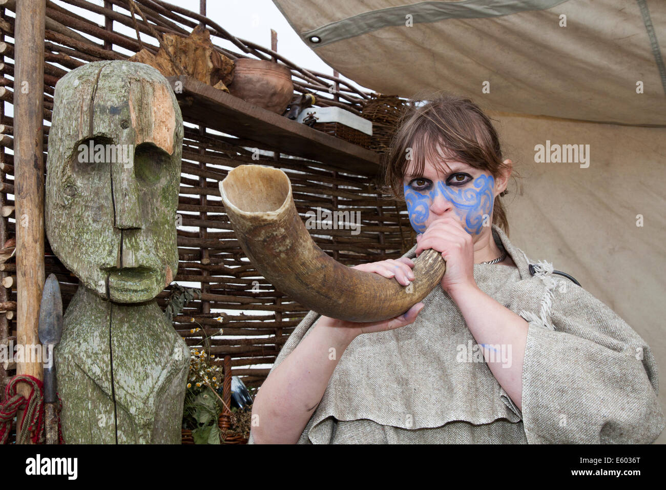 Viking woman with dyed face blowing down animal horn with carved human face, a wooden statue in Ardesier, Invernesshire, Scottish Homecoming Event.  Celebration of the Centuries at Fort George with living history camps outlining major periods in ancient Scotland's past. Stock Photo