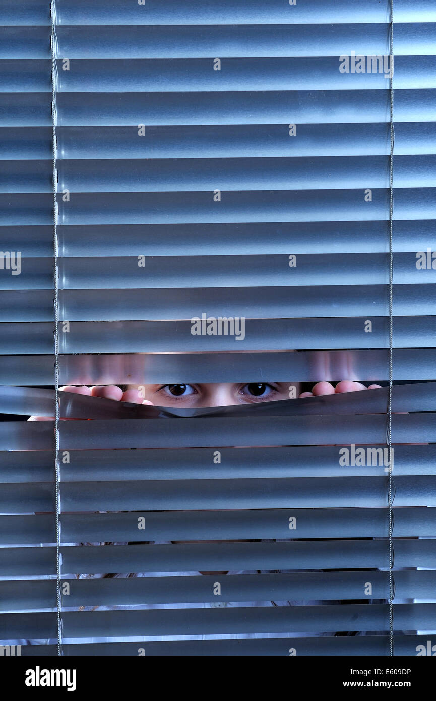 Girl's eyes looking through window blinds Stock Photo