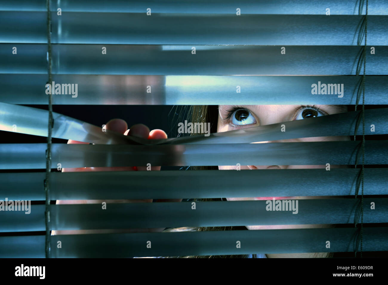 Girl's eyes looking through window blinds Stock Photo