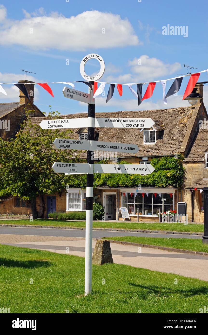 Black and white signpost on the village green along the High Street giving directions to tourist attractions, Broadway, England. Stock Photo