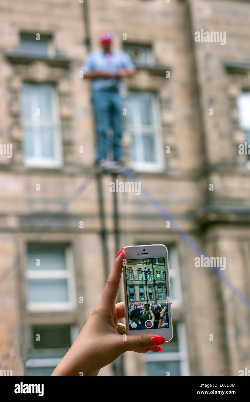 A woman's hand holding a mobile phone and recording a street performer doing a trapeze act at the Edinburgh Fringe Festival Stock Photo