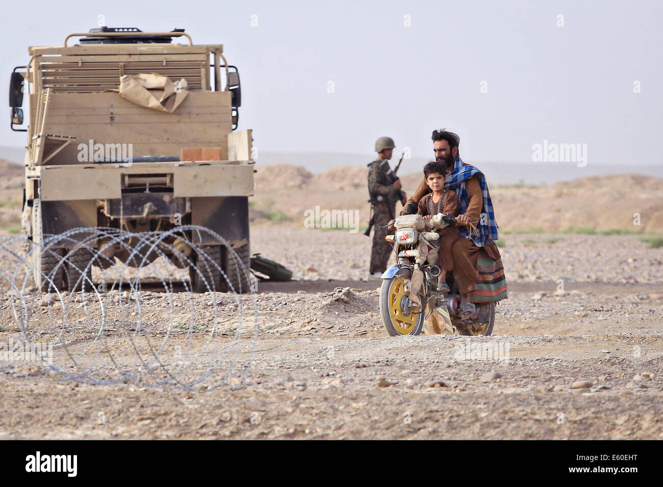 Afghan civilians ride past an Afghan National Army soldier at a vehicle checkpoint July 14, 2014 in the Shekasteh Tappeh village, Helmand province, Afghanistan, July 14, 2014. Stock Photo