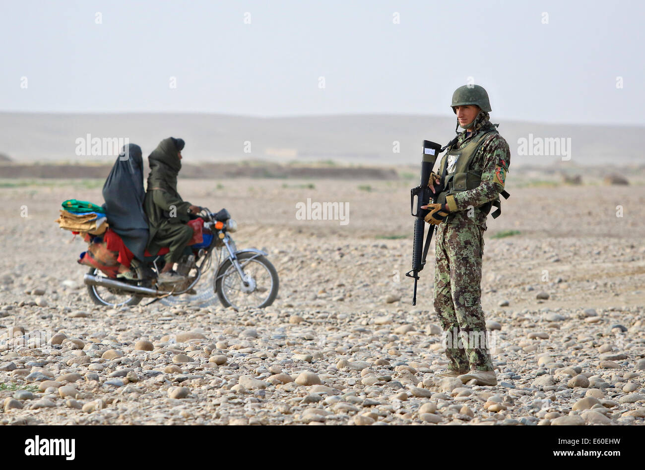 Afghan civilians ride past an Afghan National Army soldier at a vehicle checkpoint July 14, 2014 in the Shekasteh Tappeh village, Helmand province, Afghanistan, July 14, 2014. Stock Photo