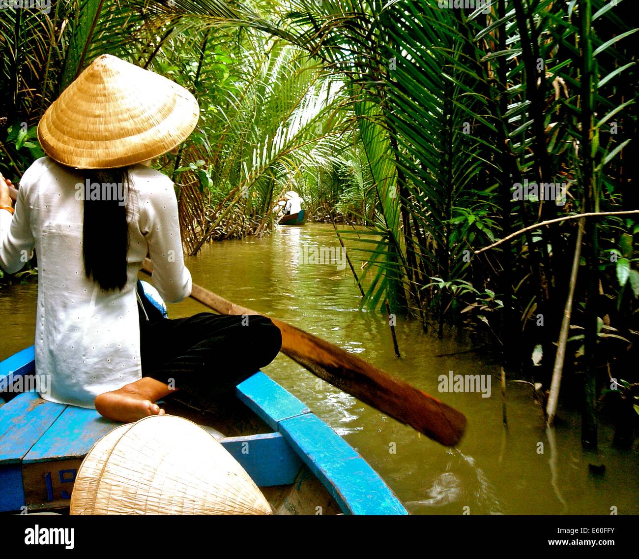 A Vietnamese lady wearing a traditional conical hat, sits on her wooden boat in the Mekong Delta, near Ho Chi Minh city, Vietnam Stock Photo