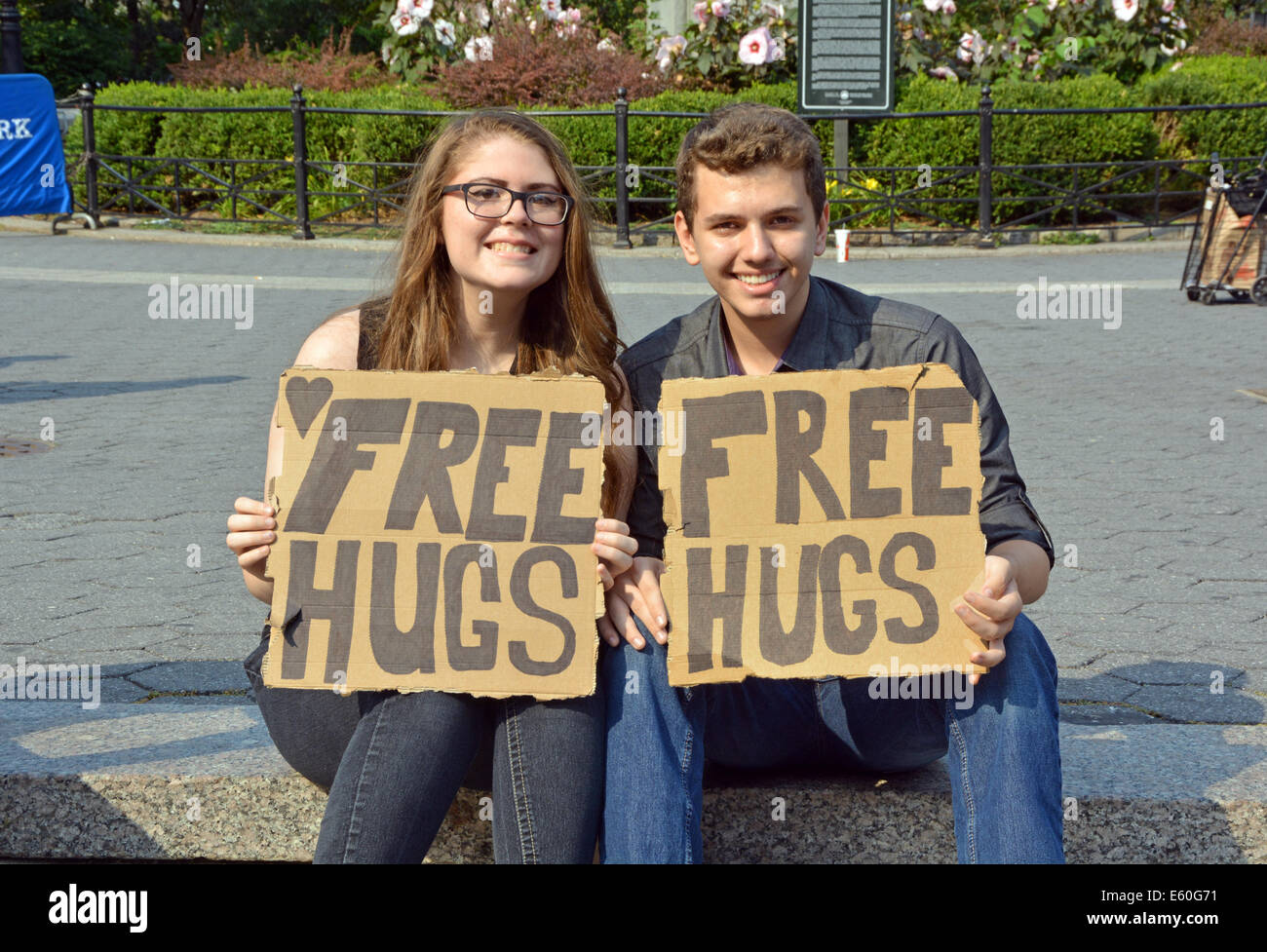 Portrait of a young man & woman holding sign saying FREE HUGS. In Union Square Park, new York City. Stock Photo
