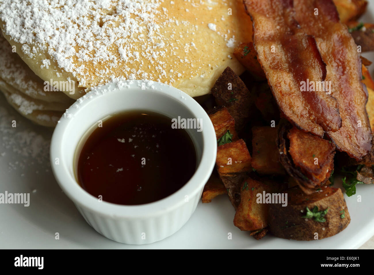 A breakfast of pancakes, crispy bacon, potatoes and maple syrup served
