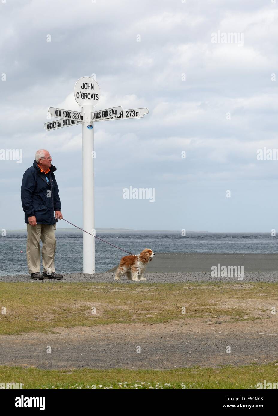 A man walks his dog past the signpost marking the end of Scottish land mass, John o' Groats, Caithness, Highlands, Scotland Stock Photo