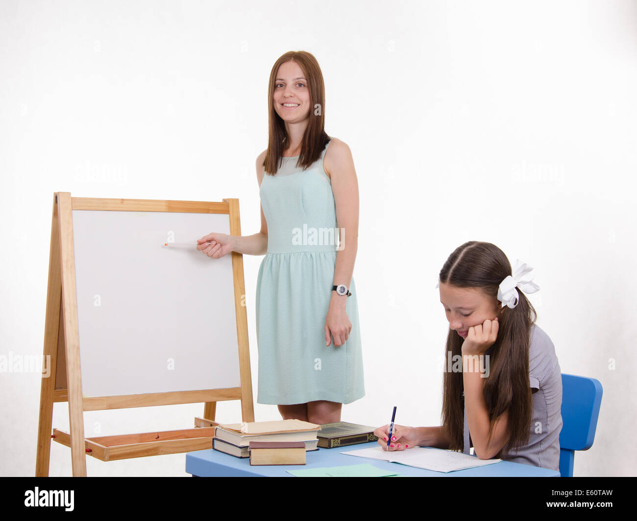 The teacher stands at the blackboard, a student sitting at a desk and listening to the teacher
