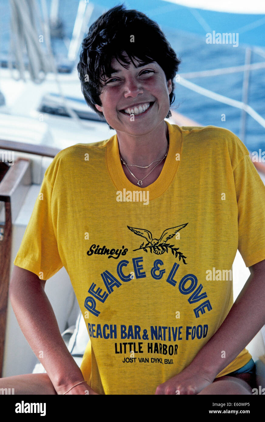 A smiling sailor proudly displays her souvenir T-shirt from Sidney's Peace & Love Beach Bar on Jost Van Dyke in the British Virgin Islands (BVIs). Stock Photo
