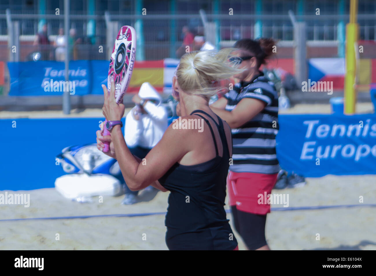 City of Brighton & Hove, East Sussex, UK. European Beach Tennis Championships 2014 Brighton, Yellow Wave, Madeira Drive, Brighton, Sussex, UK. In this image the women's doubles team from Hungary take shelter behind their rackets from the wind blowing through court 1. 10th August 2014 Stock Photo