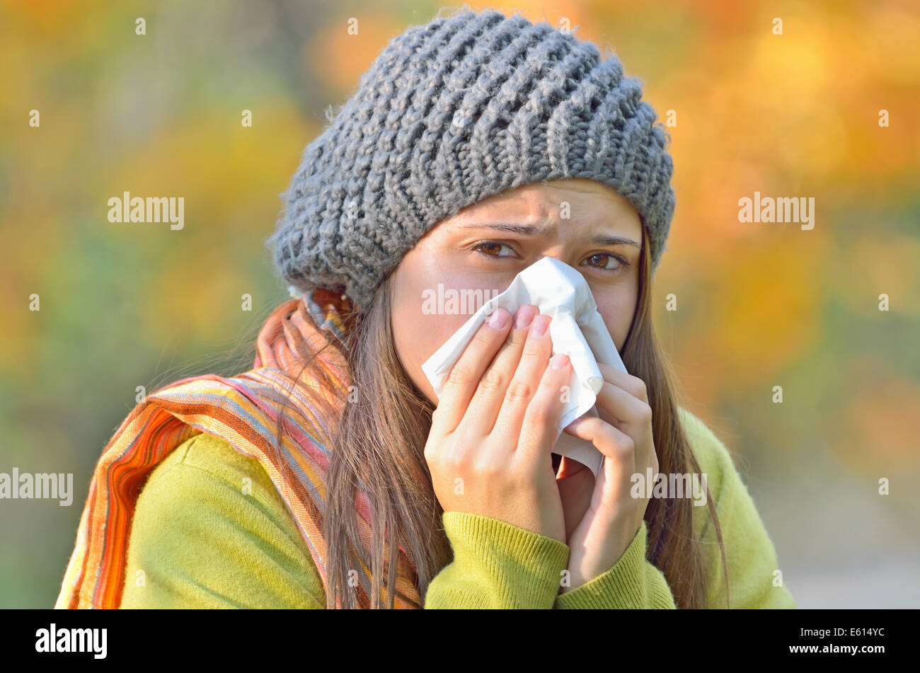 Sick young model isolated on autumn background blowing her nose Stock Photo