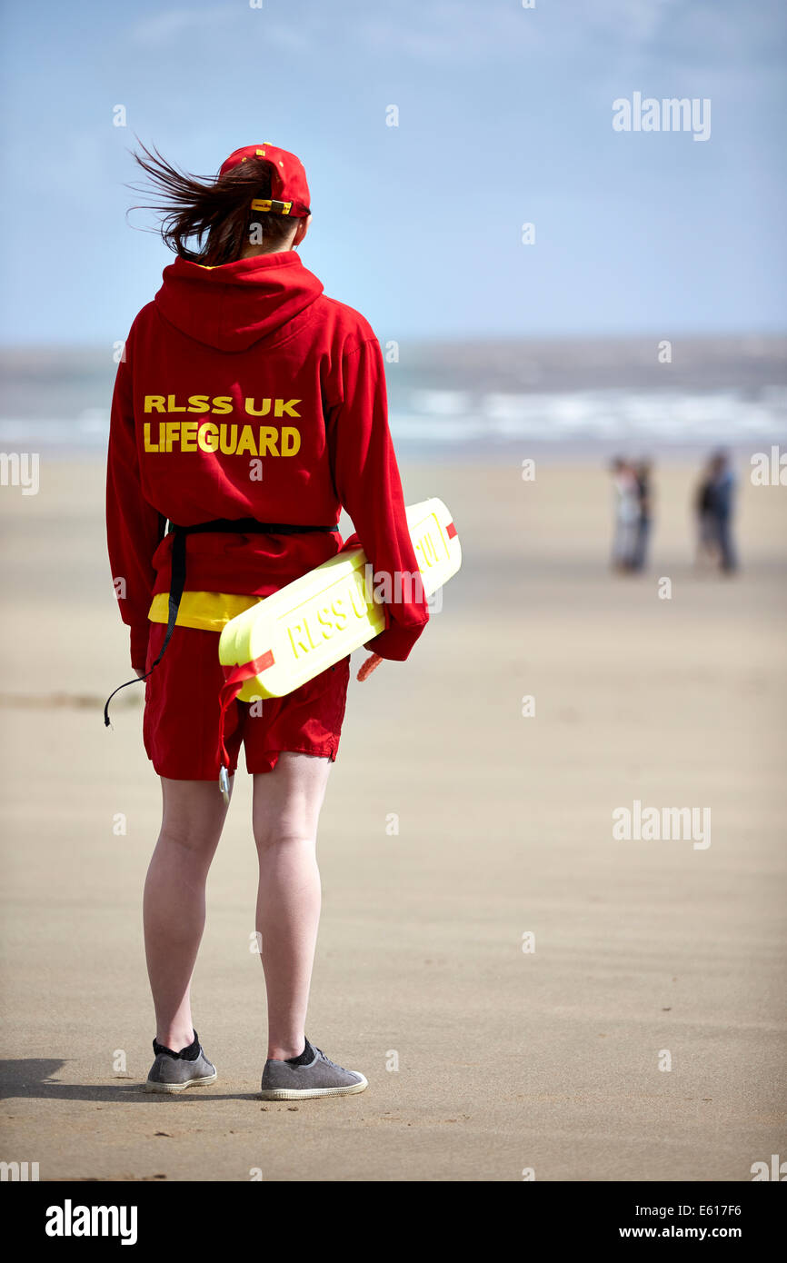 A RLSS or Royal Life Saving life guard stands watch near to the sea on a beach. Life guards help prevent drowning in the water. Stock Photo
