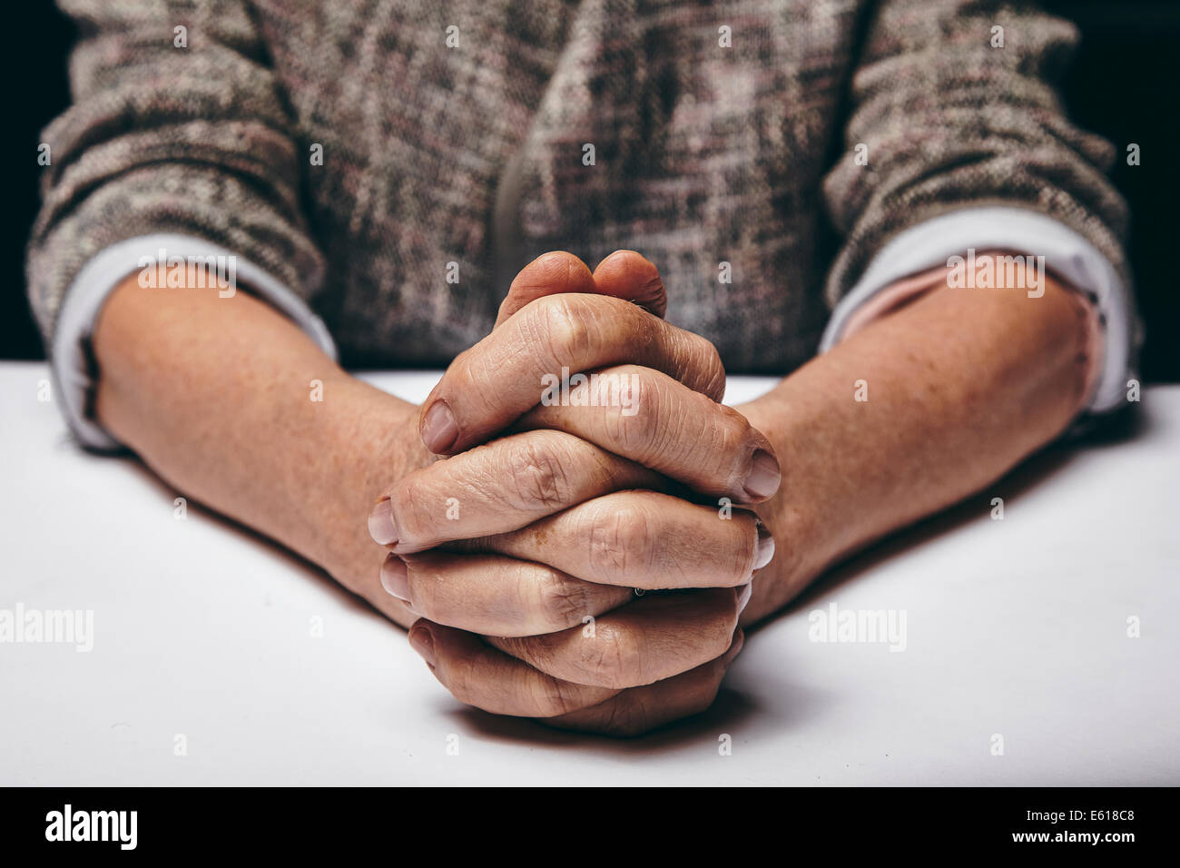 Studio photography of praying hands of a senior woman on table. Old hands clasped on a table. Stock Photo