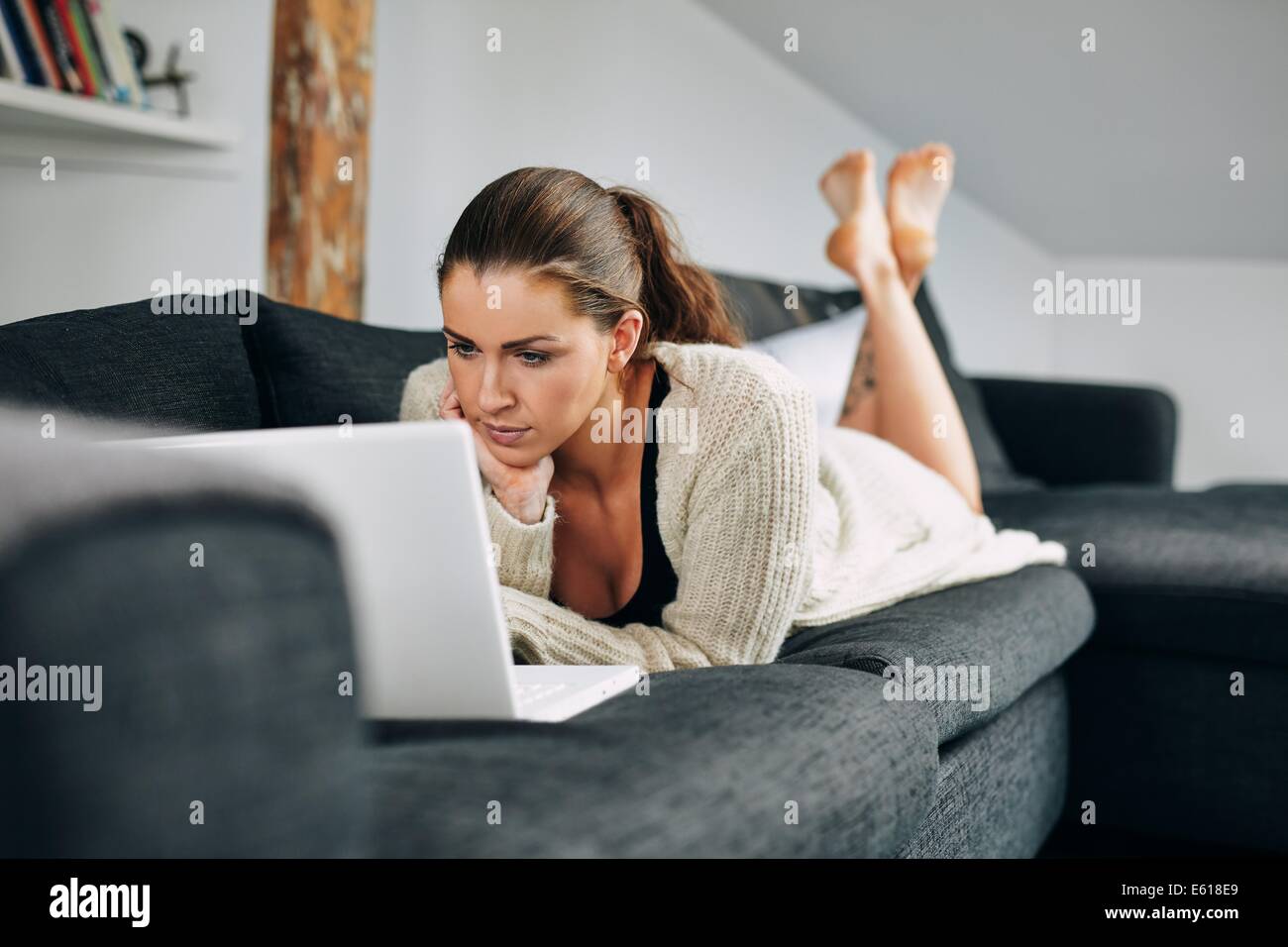 Portrait of beautiful young woman working on laptop while lying on sofa. Female using laptop at home. Stock Photo