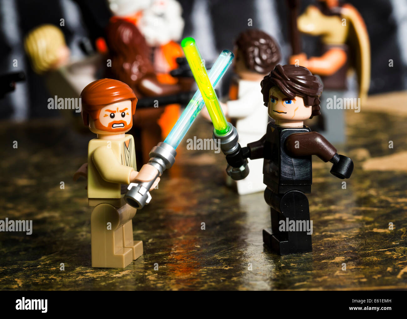 Lego Star Wars figures of Obi Wan Kenobi and Anakin Skywalker facing each other with lightsabers. other figures behind Stock Photo