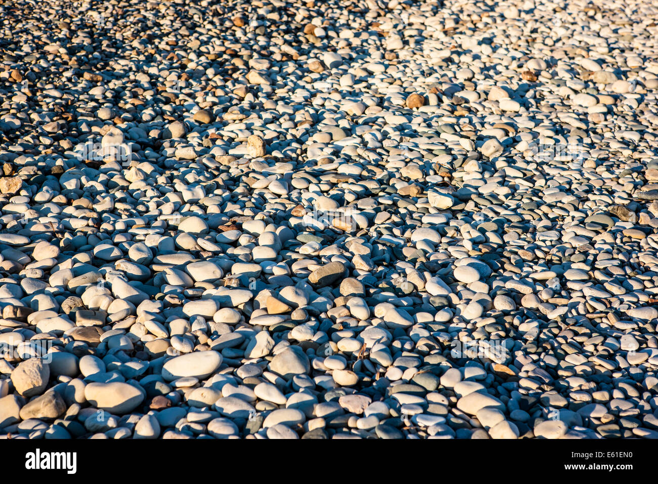 a beach covered in pebbles lit by warm sunlight Stock Photo