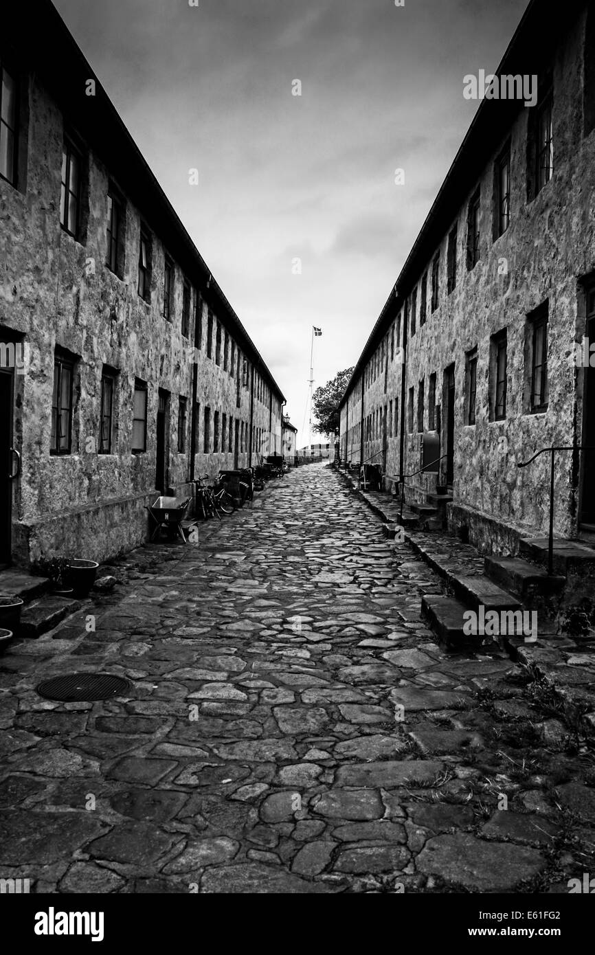 A narrow cobbled street between 2 rows of terraced houses with a Danish flag flying on a flagpole at the very end of the street Stock Photo