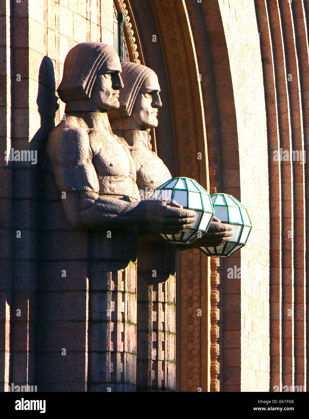 Stone guardian statues sculpted from Finnish granite holding light globes looking out from the side of Helsinki railway station Stock Photo