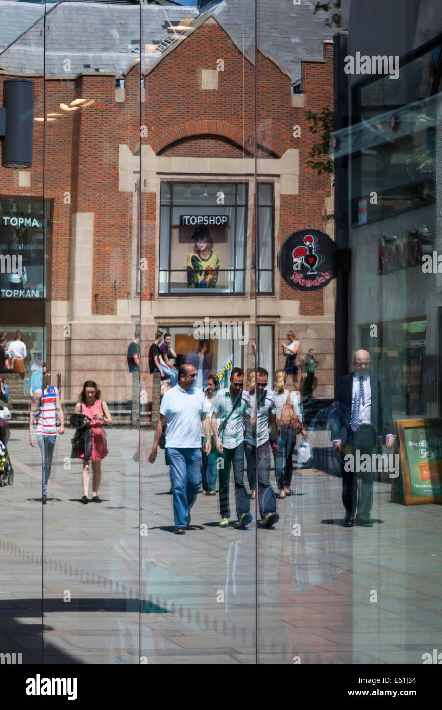 Shoppers walking along the pavement with the Friary shopping centre in the background, all reflected in a shop window. Stock Photo