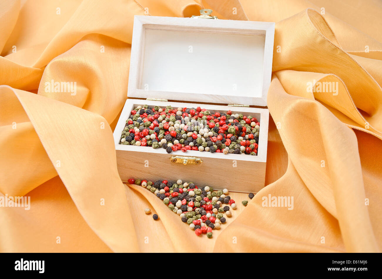 Pepper Treasure - Mixed dried peppercorns in a wooden box on cream colored silk. Stock Photo