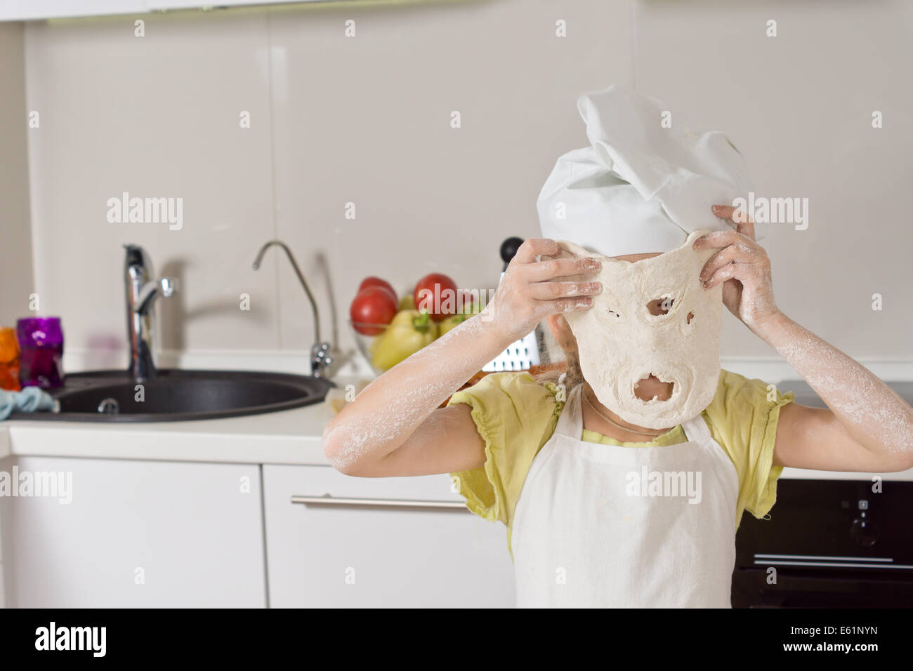 Little girl playing with a dough mask holding up a freshly rolled out portion of pastry through which she has punched a mouth and nose. Stock Photo