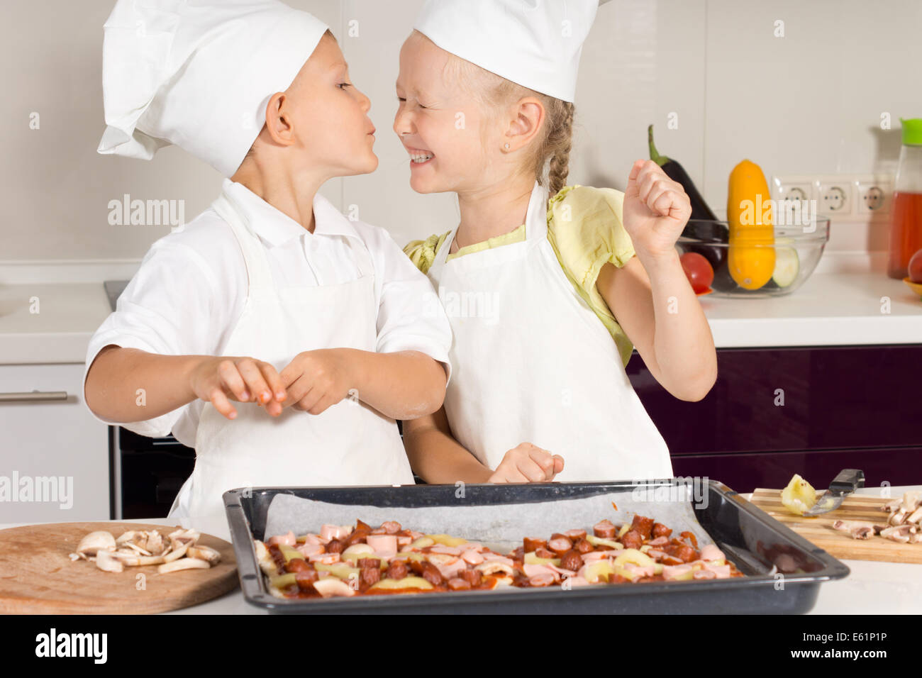 Cute Little Chef Kissing her Chef Sister in the Kitchen. Very Happy Kids. Stock Photo