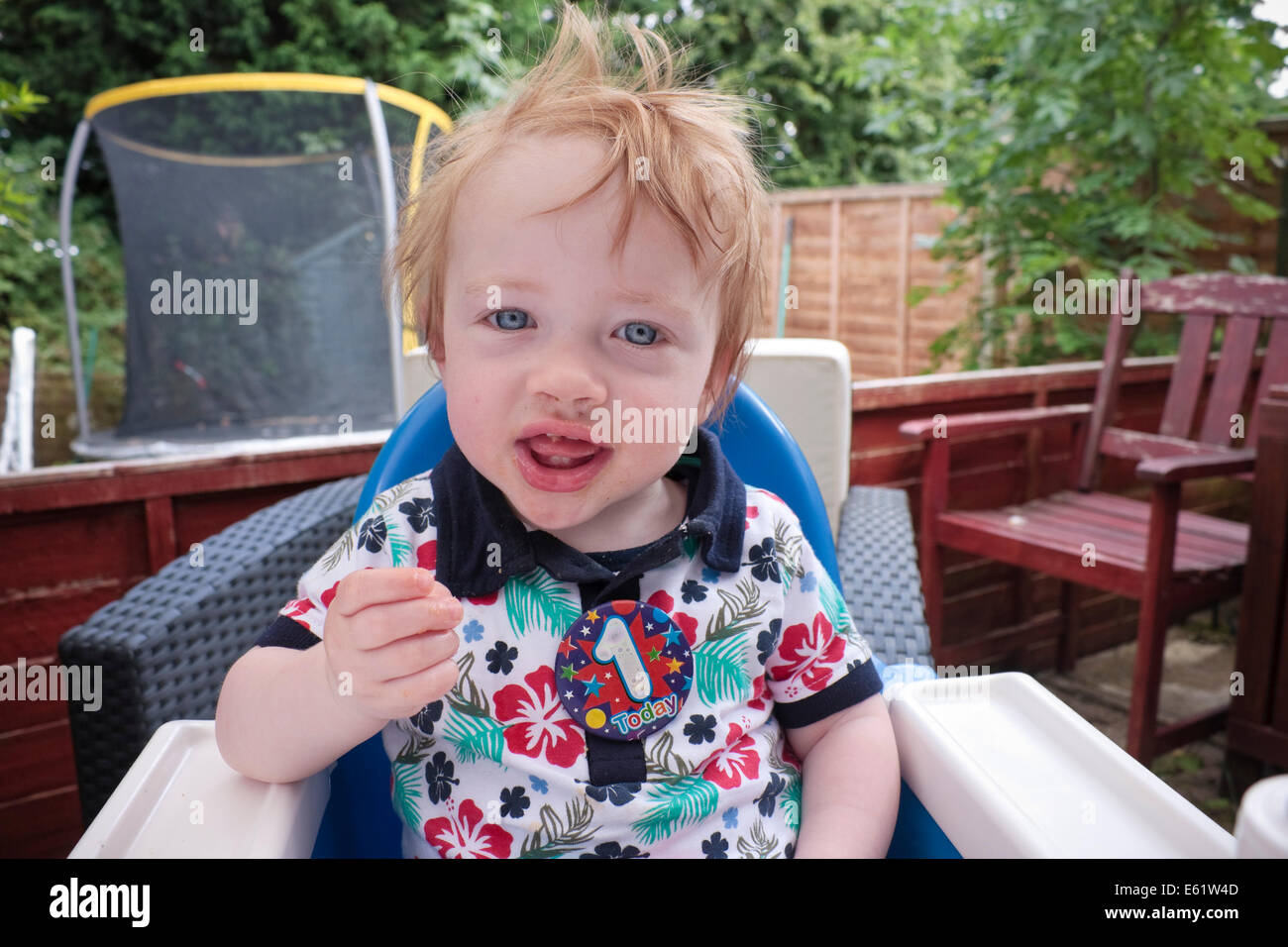 A one year old boy sitting in a highchair eating crisps Stock Photo