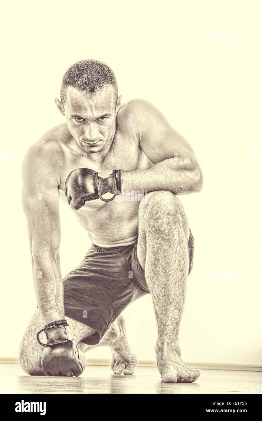 serious and concentrated martial fighter with fight gloves pray for victory while kneeling down and looking at camera Stock Photo