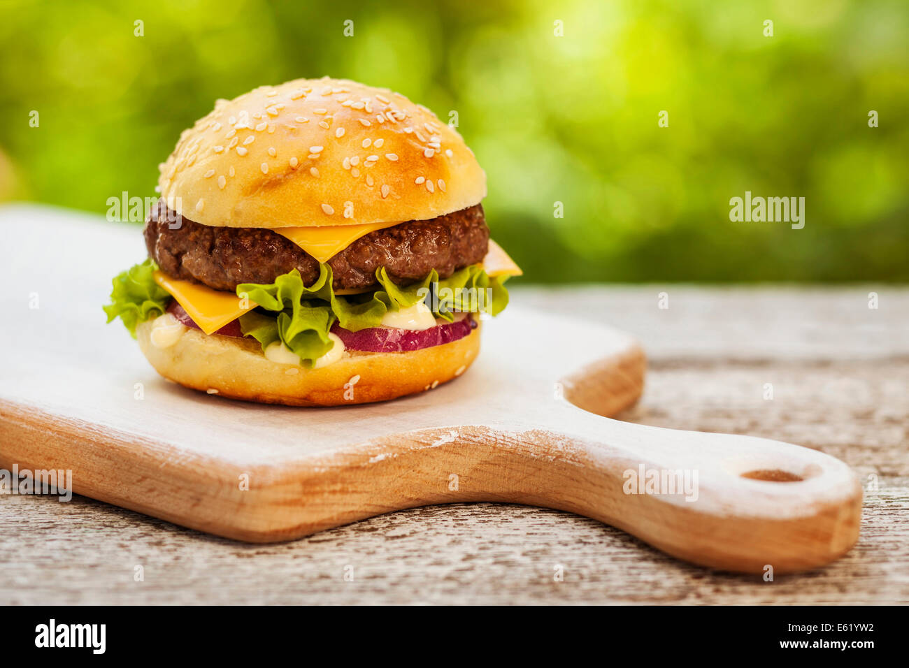 Tasty burger with cheese, lettuce, onion and tomatoes served outdoor on a wooden table Stock Photo