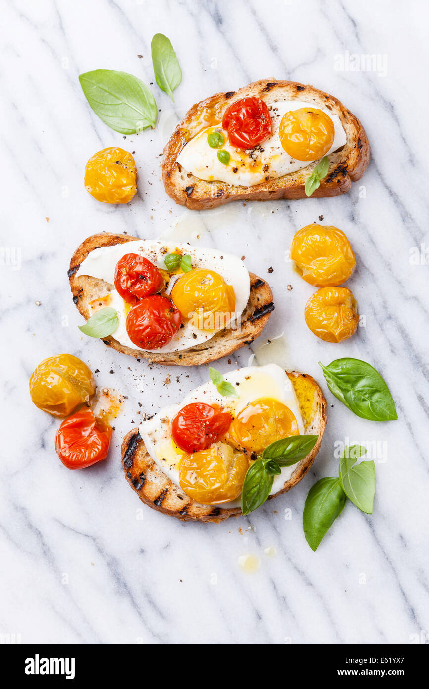 Bruschetta with roasted tomatoes and mozzarella cheese on grilled crusty bread on white marble Stock Photo