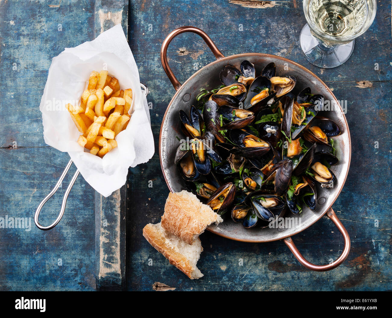 Mussels in copper cooking dish and french fries on blue background Stock Photo
