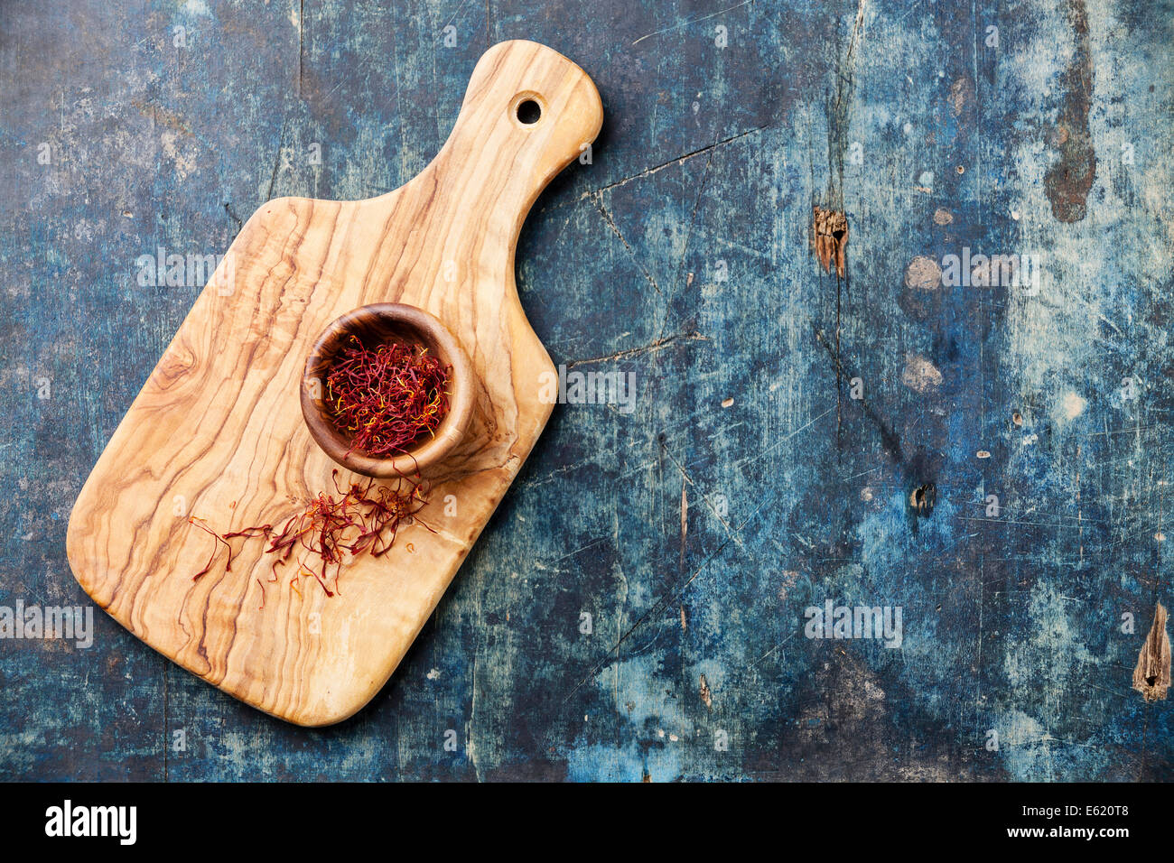 Saffron in olive wood bowl on blue wooden background Stock Photo