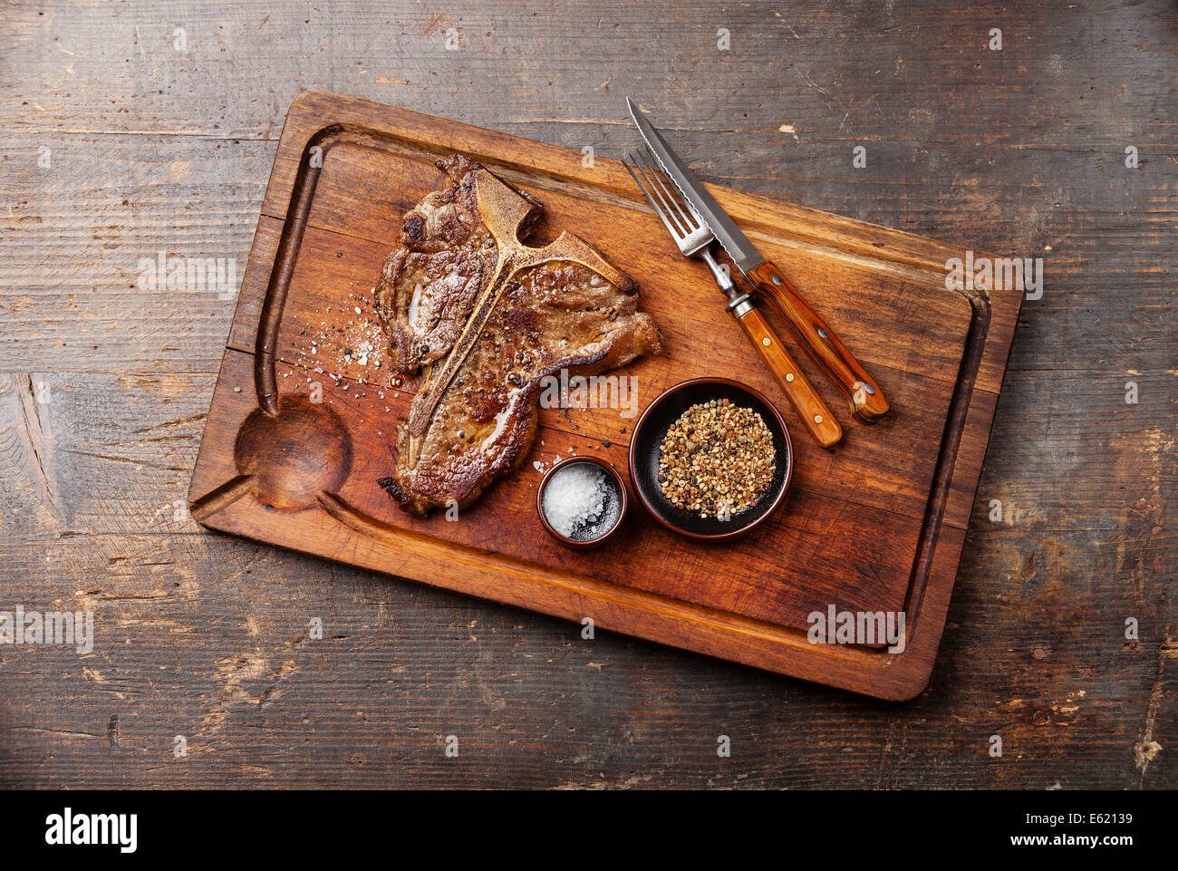 Grilled TBone Steak with salt and pepper on meat cutting board on dark