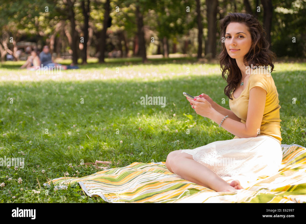Portrait of a beautiful young woman sitting on the grass at park and ...