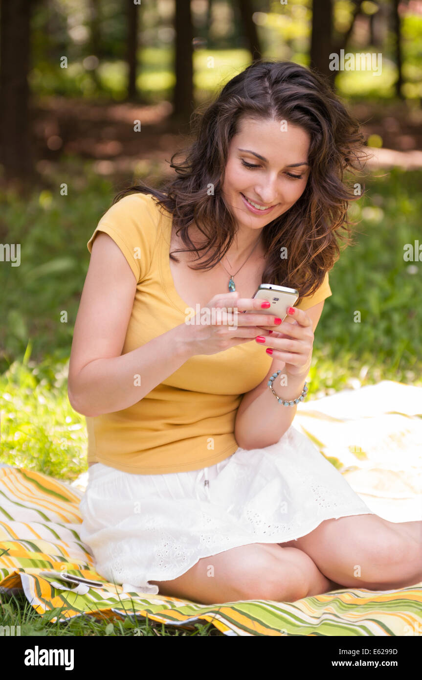 Portrait of a beautiful young woman sitting on the grass at park and ...