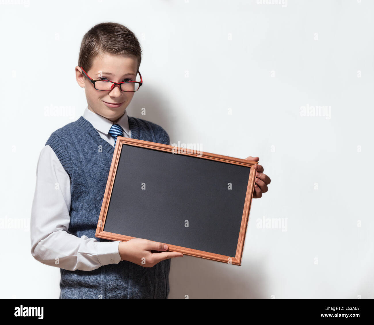 The cute smart schoolboy teenager in a glasses shows the empty black chalkboard with the place for text Stock Photo