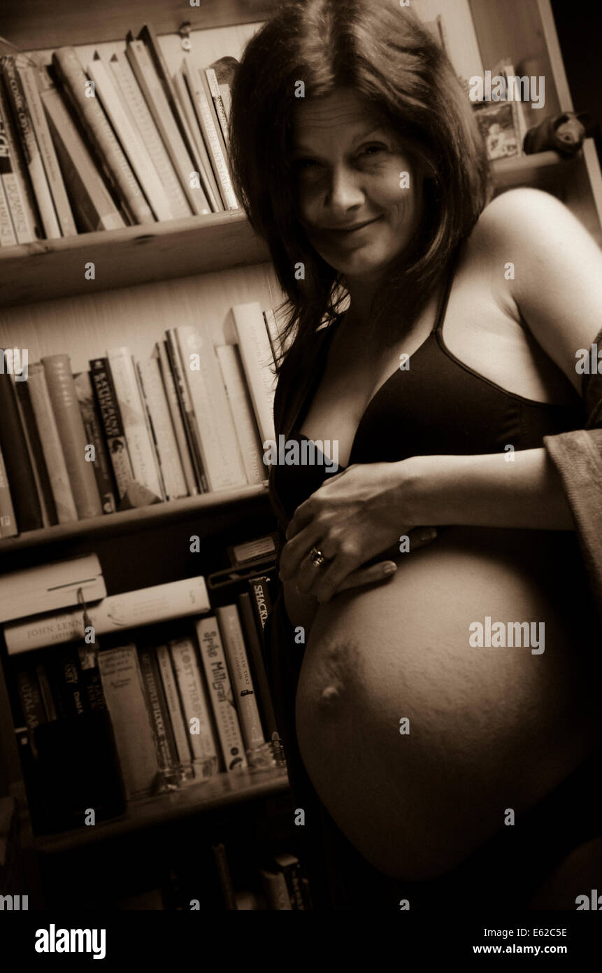 smiling pregnant woman with bookshelf in background Stock Photo