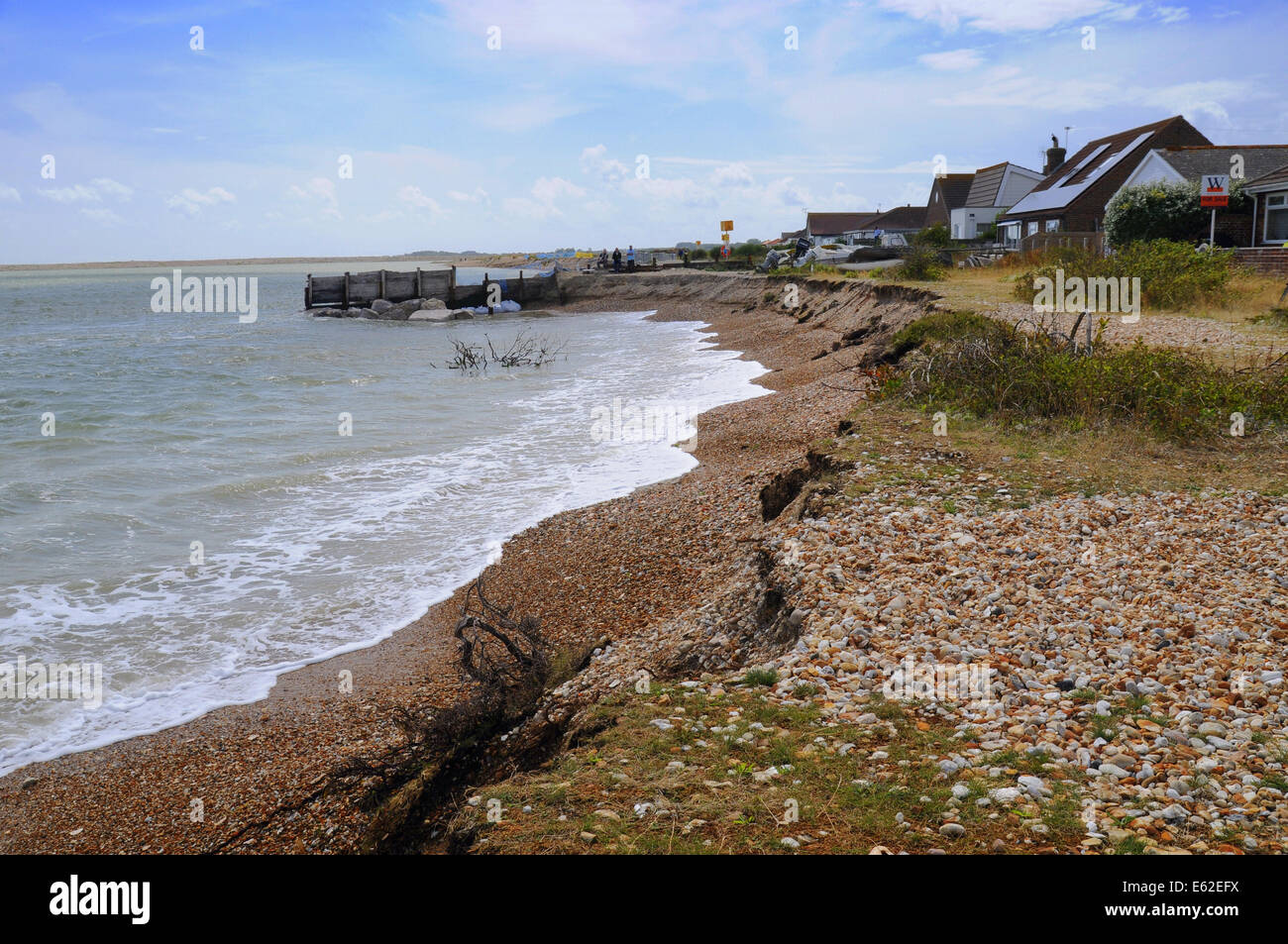 Pagham, West Sussex, UK.12 August 2014.Coastal erosion continues along the South Coast, accelerated by recent unseasonal storms. Bungalows on the beach at Pagham are now close to the advancing sea. Efforts are being made by Adur District Council to protect the properties, lorries evident today tipping large rocks on the shingle. Some locals are saying it is too little too late and believe that unless the large spit build up is breached again, as it was in the past, further erosion is inevitable. Credit:  David Burr/Alamy Live News Stock Photo